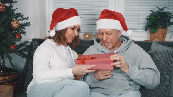 A Happy Middleaged Couple in Santa Hats Opening a Christmas Gift Box