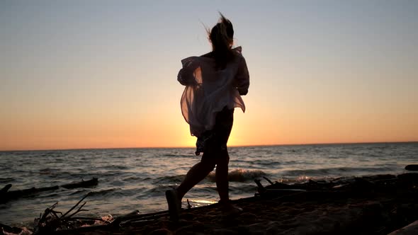 Silhouette of a Free Girl in a White Shirt Running Along the Seashore in the Sunset