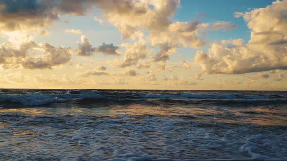 Sunset Behind Clouds Over Sea Waves and Sandy Beach