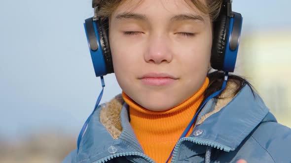 Confident Teenager Girl Listening to Rap Music Through Blue Wireless Headphones and Online