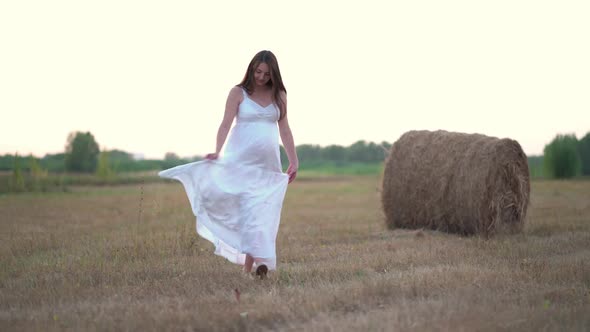 Beautiful Pregnant Woman in Wheat Field with Haystacks at Summer Day