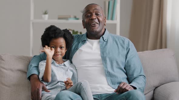 African American Family Sitting on Sofa Kid Girl Waving Hello Greeting Adult Father Hugging Daughter