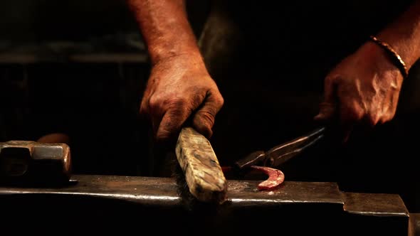 Mid-section of blacksmith using wire brush on horseshoe