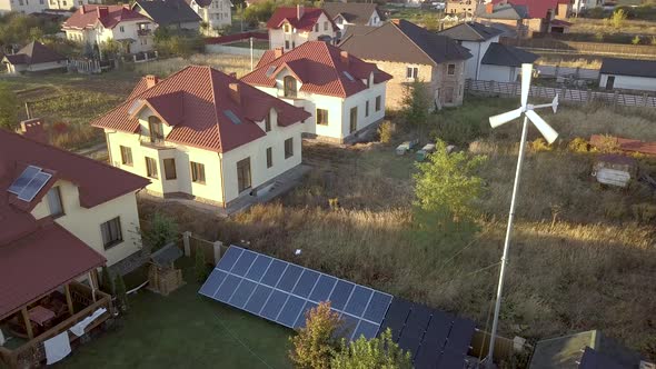 Aerial view of a residential private house with solar panels on roof and wind generator turbine