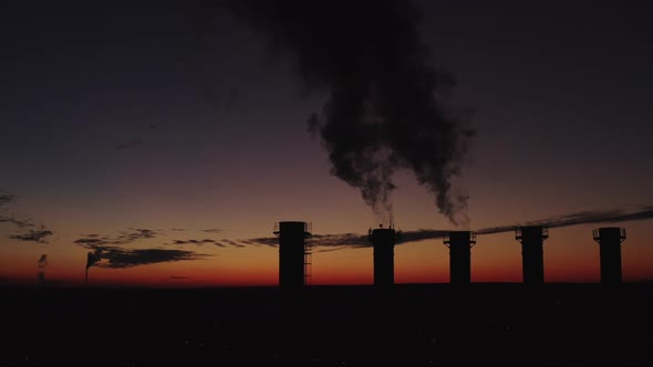 High Chimneys Against the Backdrop of the Sunset and the City. Thick Smoke Rises High. Silhouette