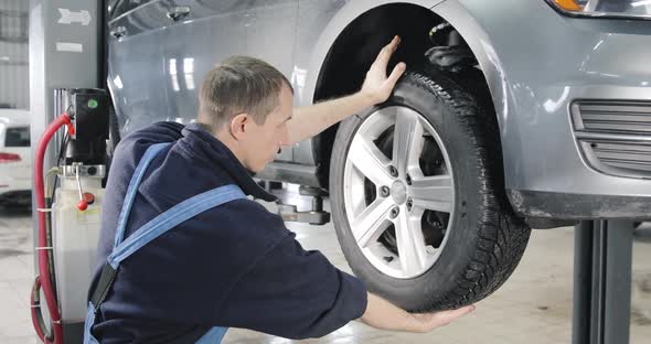 Car Raised On Lift On Car Service, Mechanic Checks Tires