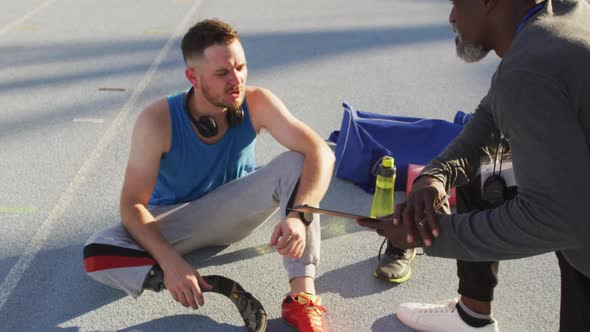 Diverse male coach and disabled athlete with prosthetic leg talking during training session