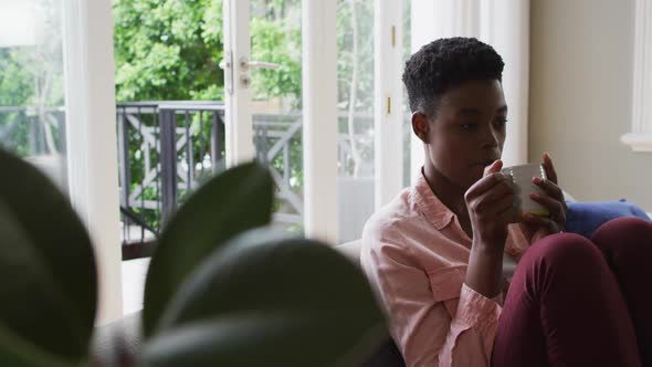 African american woman drinking coffee while sitting on the couch at home