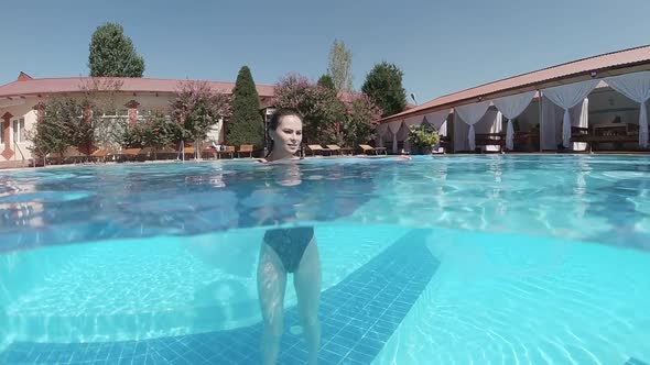 Young Woman Dressed in a Black Swimsuit Stands at the Bottom of the Swimming Pool