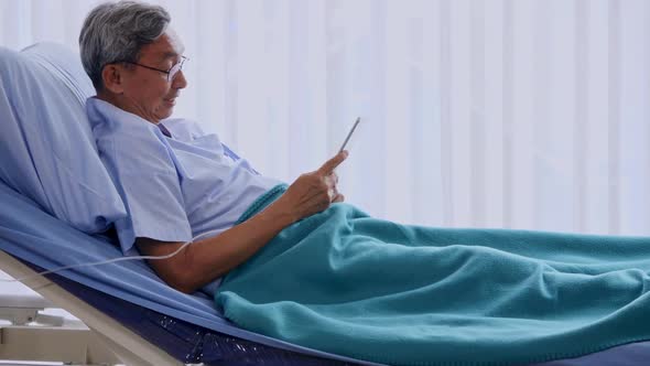 Happy elderly patient using tablet on bed at hospital
