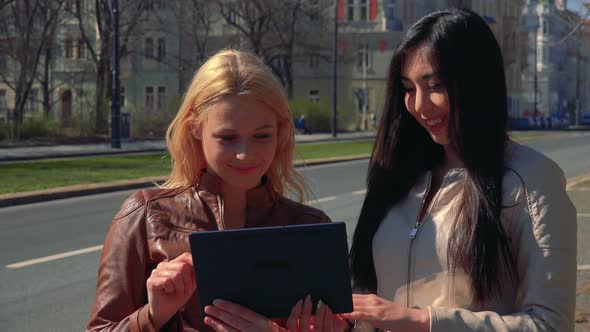 A Young Caucasian Woman Explains Something About a Tablet To a Young Asian Woman - an Urban Area