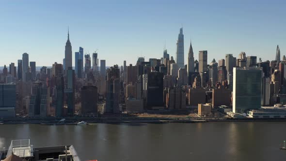 A high angle, aerial view over a calm East River on a sunny day with blue skies. The drone camera fa