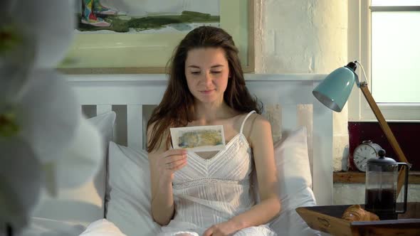 Woman sitting in bed with postcard