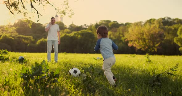 Young Father with His Little Son Playing Football on Football Pitch