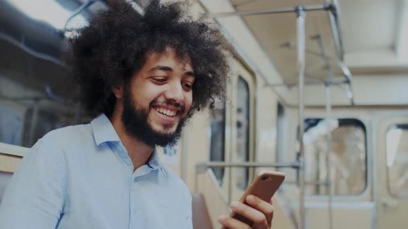 Overjoyed Curly Stylish Man with Dark Skin Using Smartphone in Subway or Underground Railway