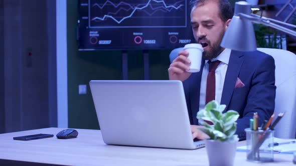 Tired Businessman Drinks Coffee While Working on the Laptop