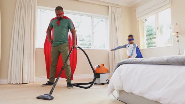 Father and son cleaning room with vacuum cleaner while pretending to be superhero 