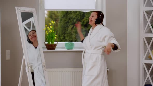 Side View Excited Carefree Mature Woman in Headphones Dancing in Front of Mirror at Home