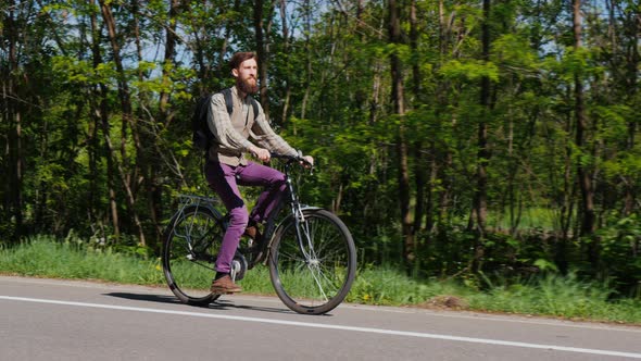 An Attractive Man with a Beard Rides a Bike Along a Bicycle Path