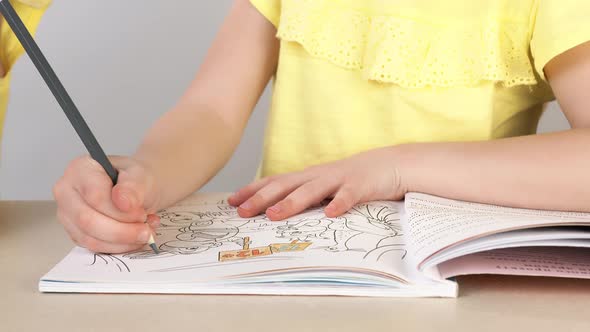 A Girl Paints a Coloring Book. Close-up of a Little Girl's Hand Holding a Pencil and Drawing.