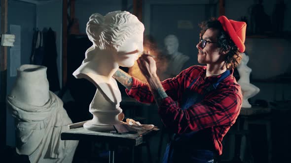 A Man is Dusting a Gypsum Bust with a Brush