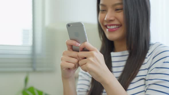 Asian beautiful woman sit on sofa and chat on mobile phone in house.