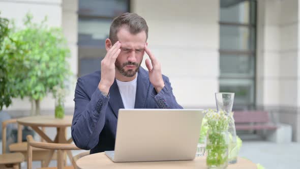 Man with Headache Working on Laptop Sitting in Outdoor Cafe