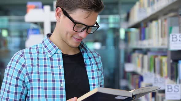 Student At Library Reading Books Near Bookshelves