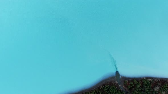 Overhead drone shot of lake water with a piece of forest on the shore in Kenai Lake, Alaska, USA