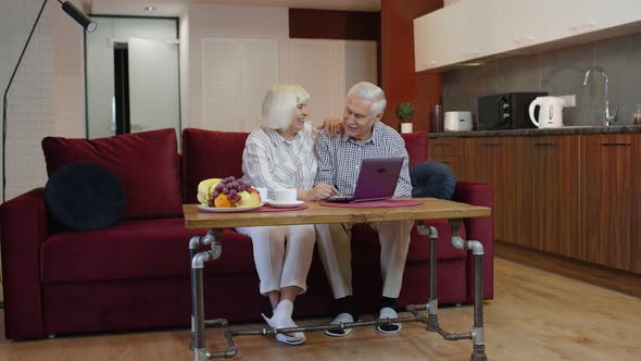 Senior Old Couple Grandparents Talking and Using Digital Laptop Computer at Home. Internet Shopping