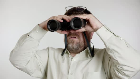 Middle aged man in green shirt looks ahead through binoculars.