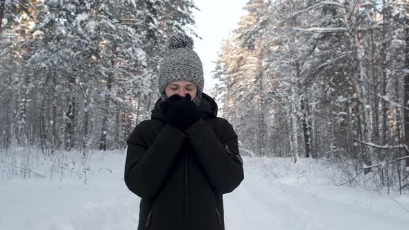 young man froze in snow forest. warms his hands in black mittens.