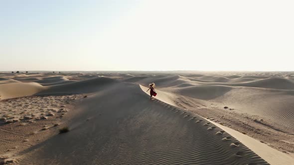 Aerial Footage of a Young Woman in Red Dress Running on a Sand Dune Desert