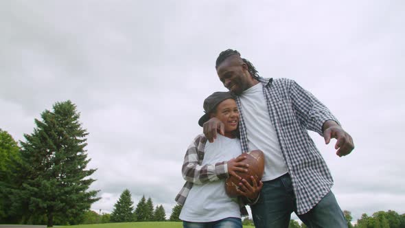 Happy Black Son and Dad with American Football Walking Outdoors