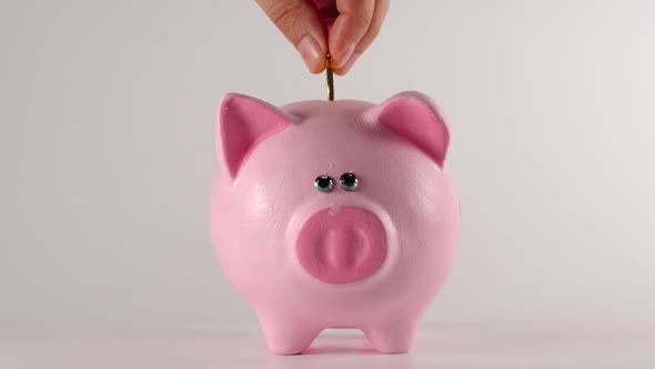 Male hand throws metal golden coin into a pink piggy moneybox