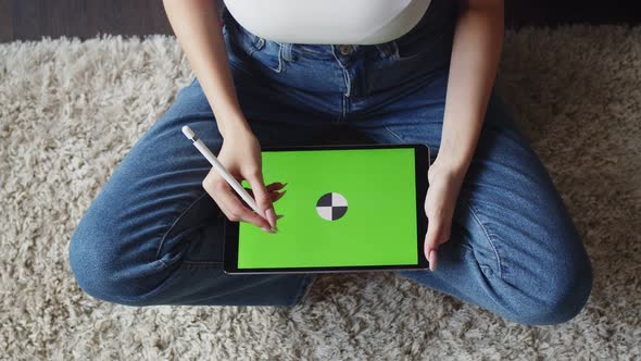 Woman Sits in Lotus Position and Draws with Stylus on Electronic Tablet with Green Screen Top View