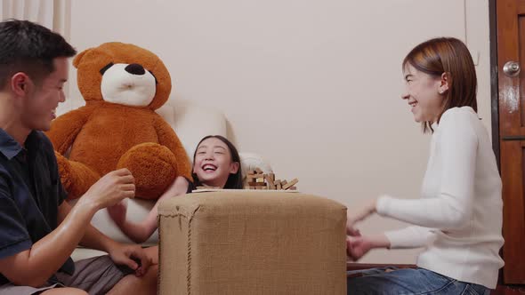 Asian mother, father, and pretty daughter playing wooden block tower together