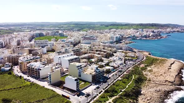 Coastal city of St. Paul Bay in Malta island with ocean waves hitting cliffs, aerial view