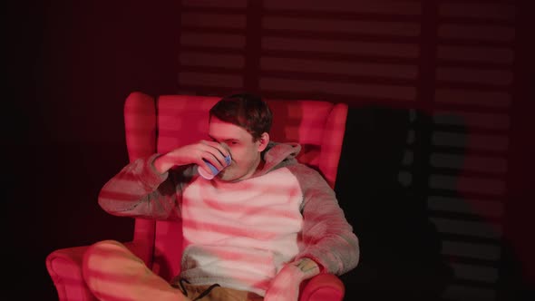 Young Man with Paper Cup of Coffee Sitting in Armchair with Incident Light From Window Through