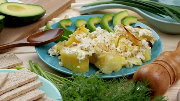 Baked Potatoes with Cheese with Slices of Avocado and Fresh Herbs on a Blue Plate on a Wooden Table