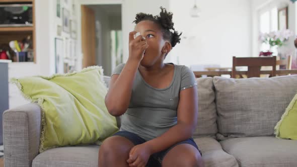 African american girl sitting on sofa in living room using inhaler