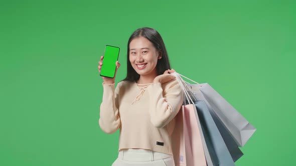 Asian Shopping Woman Holding Green Screen Mobile Phone And Shopping Bags In Front Of Green Screen