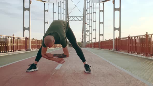 Young White Man in Black Sport Uniform Doing Warmup Before Run Pedestrian Bridge at Dawn