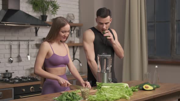 muscular young couple cooking healthy cocktail after workout, talking and laughing in the kitchen. 