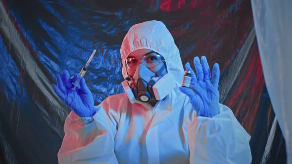 Healthcare Worker in PPE Suit Holding a Syringe and Showing a Bottle of Covid19 Vaccine