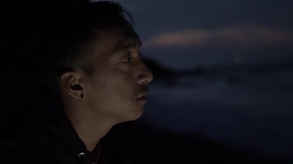 Nepalese man sits on beach at night alone smoking cigarette. Close up RACK FOCUS