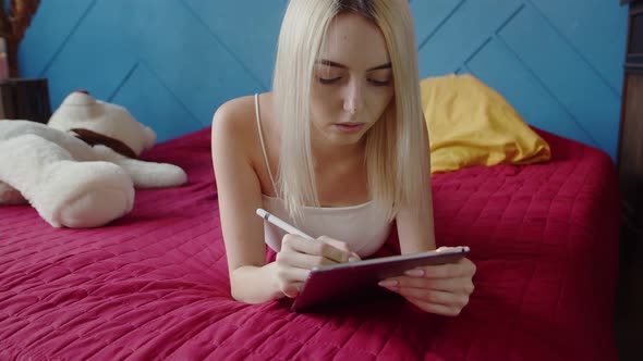 Young Woman Artist Draws Lying Bed on Graphic Tablet Using Stylus Front View