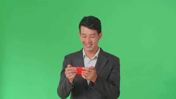 Smiling Asian Business Man Looking At The Phone Screen In Green Screen Studio