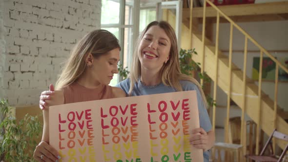 Looking to Each Other Two Handsome Young Girls are Standing in the Studio and Showing a Lgbt Poster