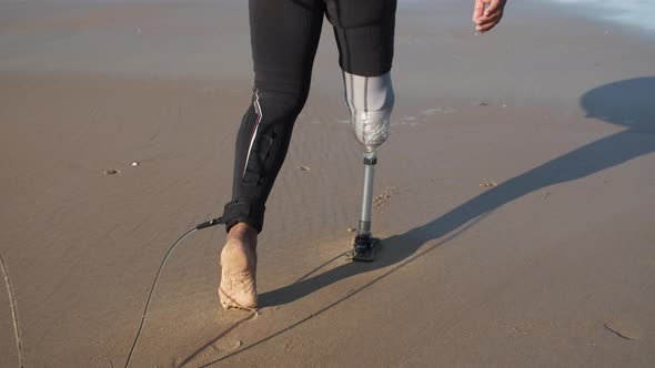 Back View of Man with Bionic Leg Going to Ocean with Surfboard